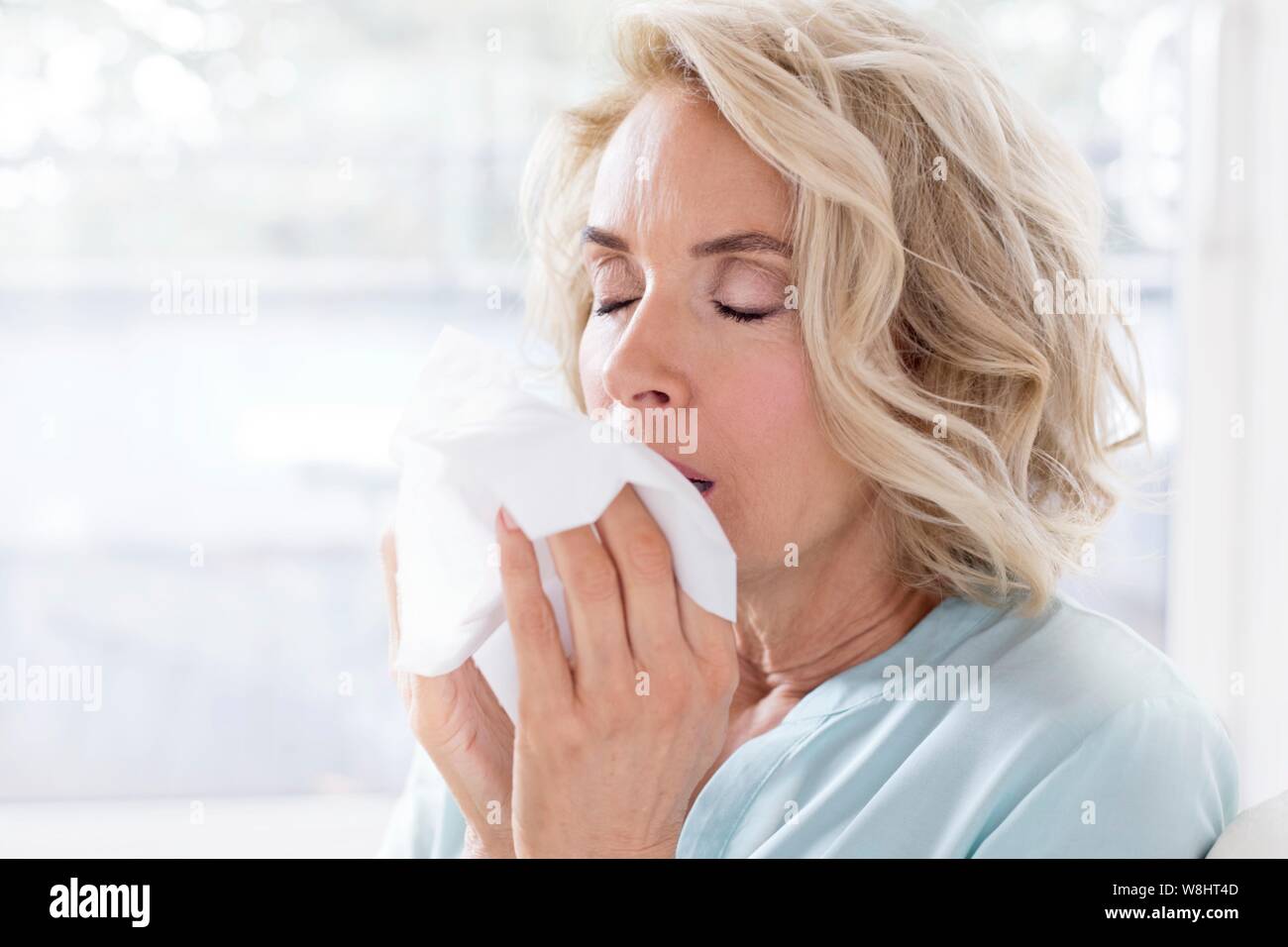 Mature woman blowing nose on tissue. Stock Photo