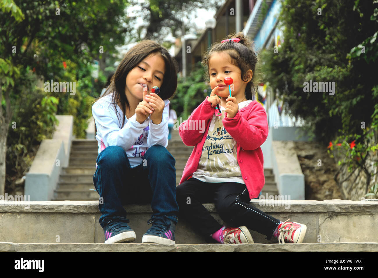 Two girls sitting and eating a lollipop in the park, summer outdoor portrait. best friends Stock Photo