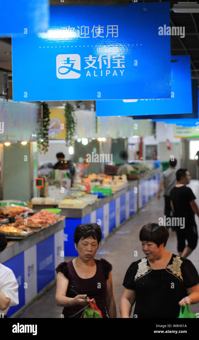 Chinese customers walk under advertisements for mobile payment service Alipay of Alibaba Group at a free market in Wenzhou city, east China's Zhejiang Stock Photo
