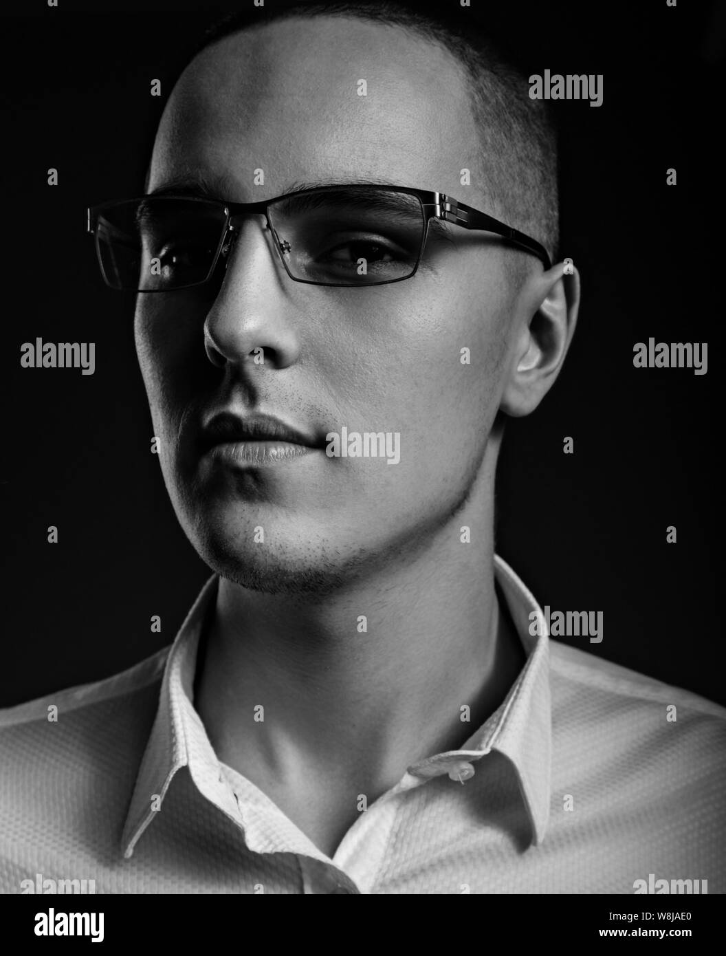 Style elegant young business man in eye glasses looking sreious and arrogant on dark shadow background. Closeup art portrait. Black and white Stock Photo