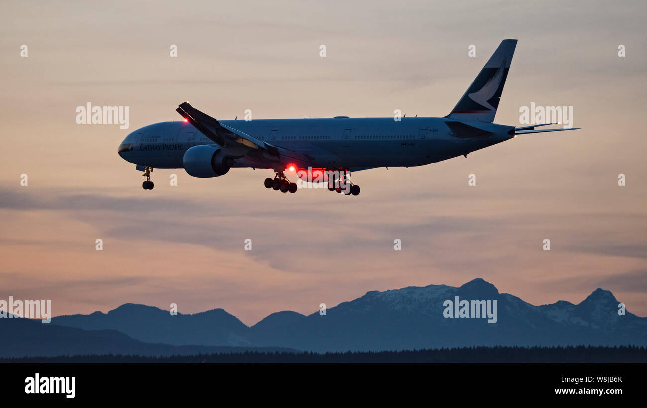 Cathay Pacific Airways plane Boeing 777-300ER airborne on short final approach for landing at sunset dusk twilight jet airliner airplane Swire Group Stock Photo