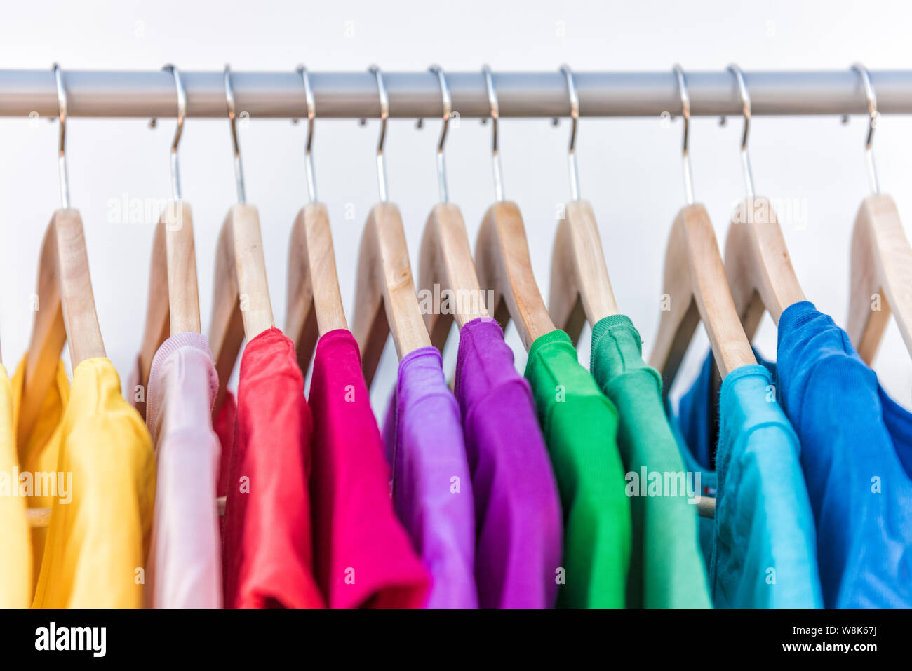Fashion clothes on clothing rack - bright colorful closet. Closeup of rainbow color choice of trendy female wear on hangers in store closet or spring cleaning concept. Summer home wardrobe. Stock Photo