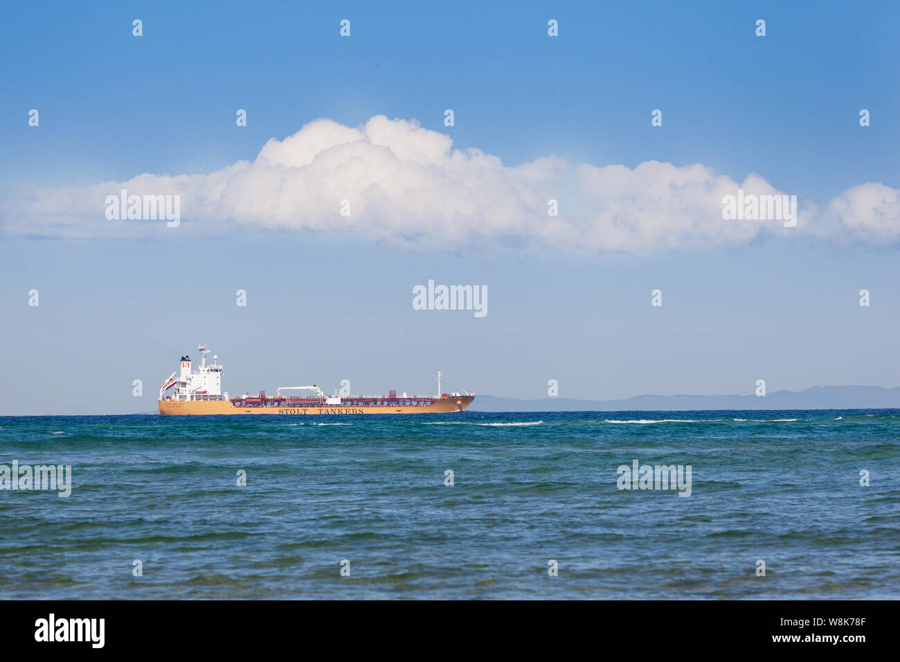 A huge yellow bulk tanker transporting goods internationally is a contrast to the blue sky and sea. Stock Photo