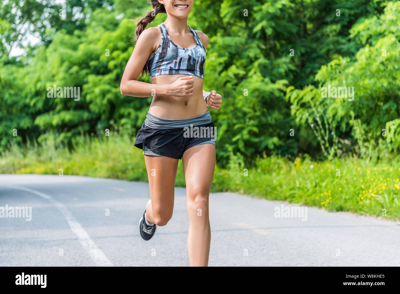 Fitness girl running in summer outdoor park. Happy fit athlete working out  in sports bra and 2-in-1 compression shorts fashion activewear outfit  showing off slim body and abs training for weight loss