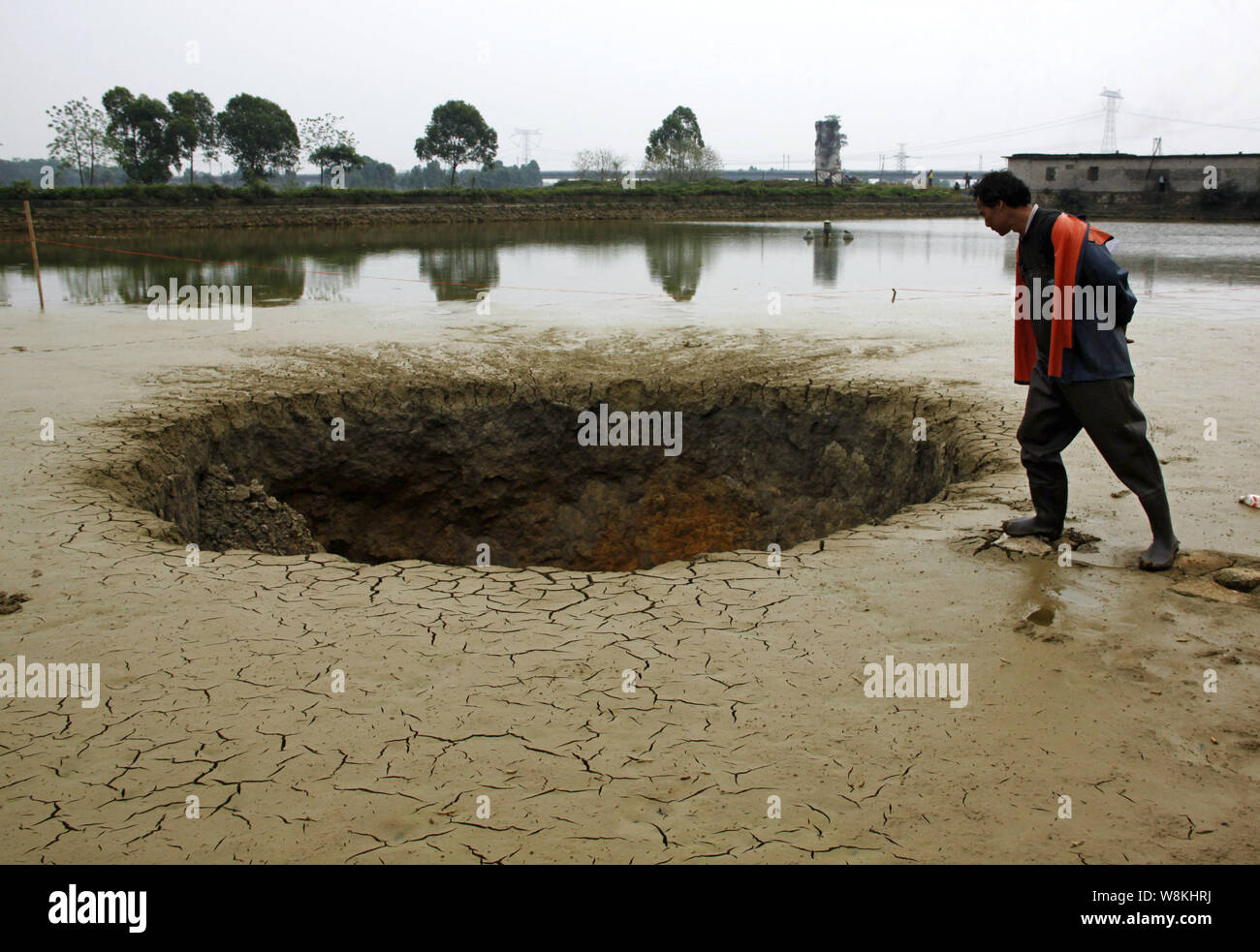 A Chinese farmer looks into the giant sinkhole in a nearly dried-up fish pond after all the fish were sucked into the hole in Baisha town, Guiping cit Stock Photo