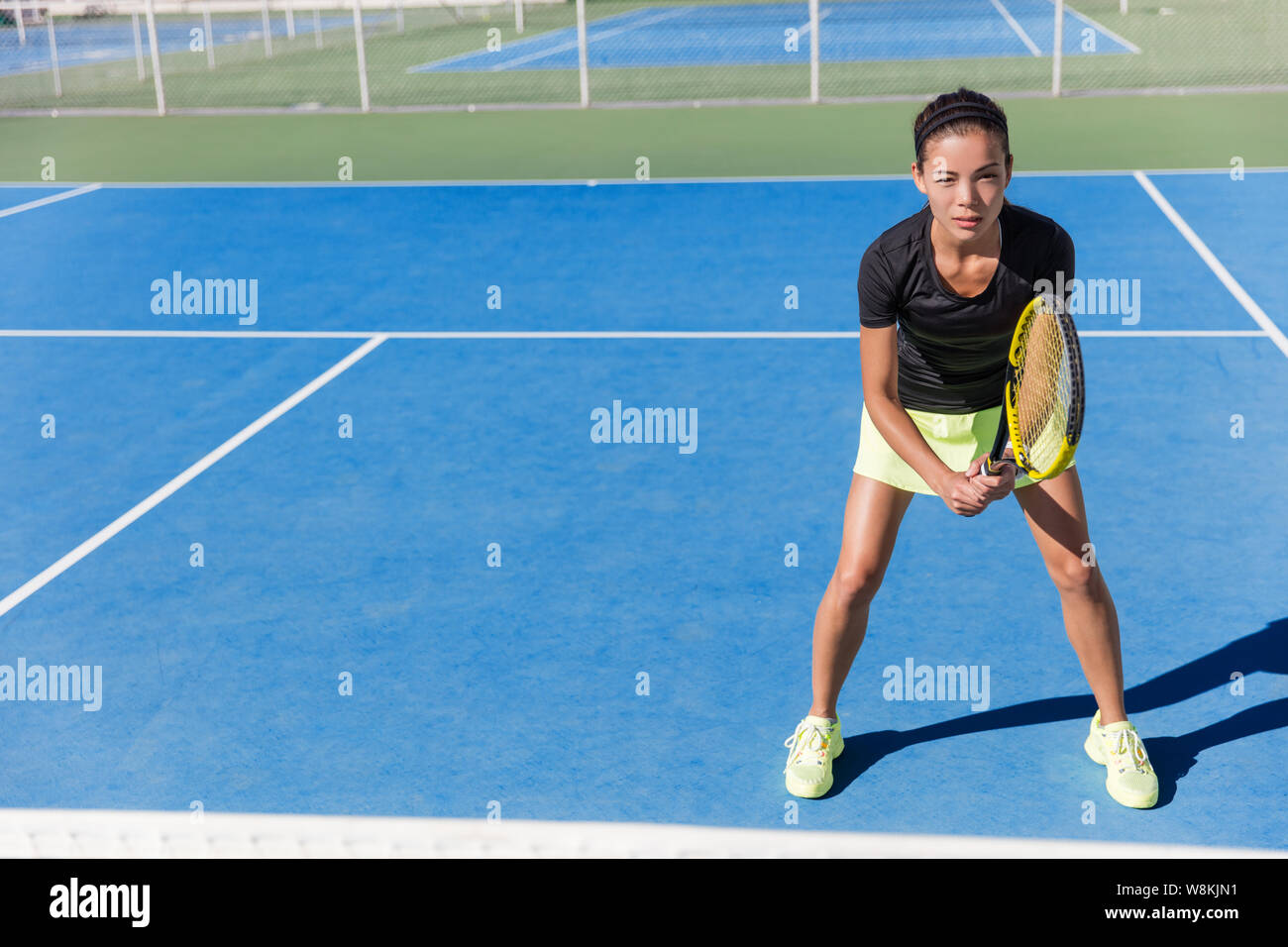 Asian tennis player woman ready to play on blue hard court outdoor in summer in position holding racket wearing outfit with skirt and shoes. Female athlete determination and concentration concept. Stock Photo