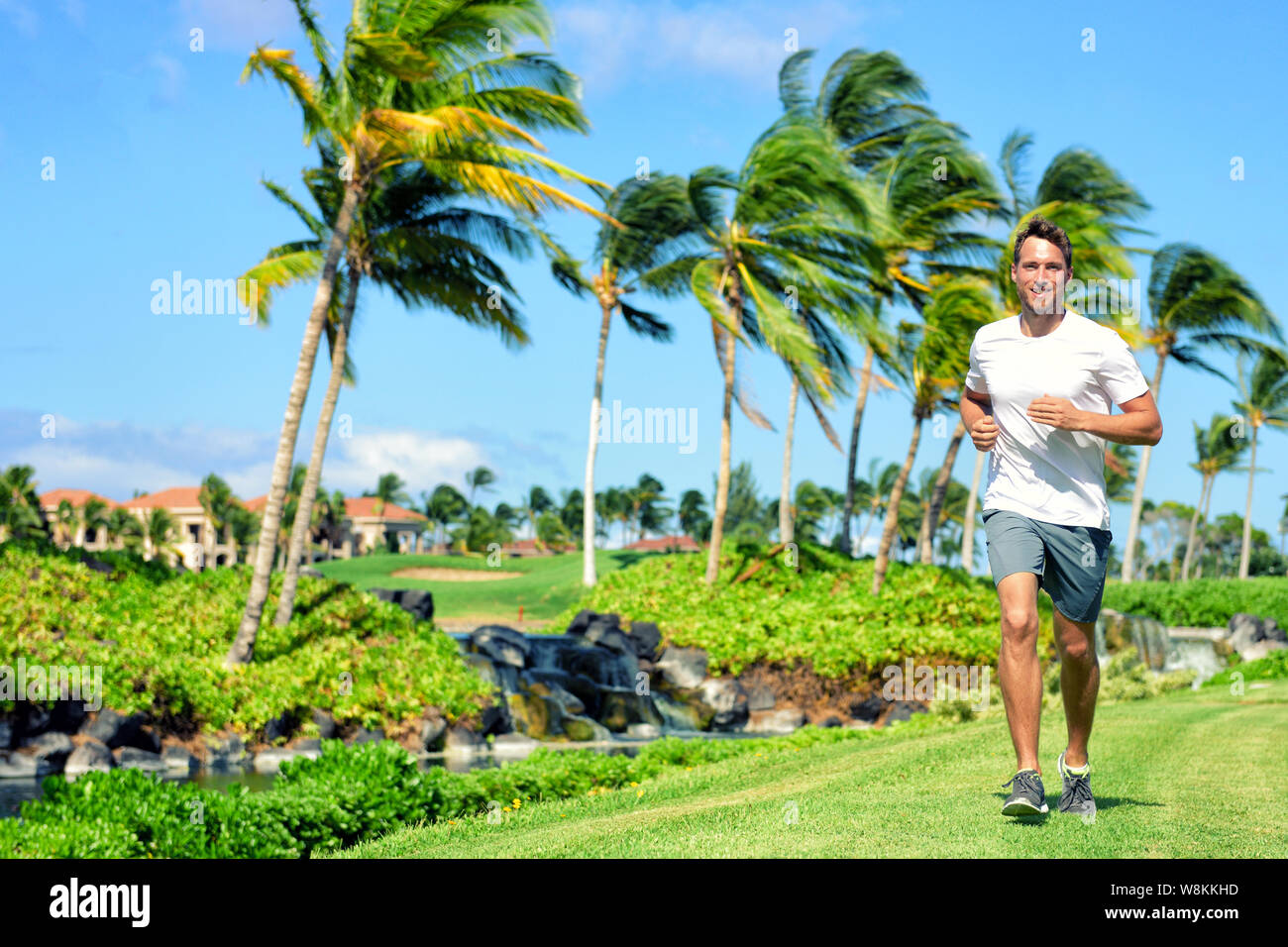 Active lifestyle man runner jogging in high end luxury residential american tropical neighborhood - Miami Florida living. Healthy running male fitness athlete working out cardio on grass in summer. Stock Photo