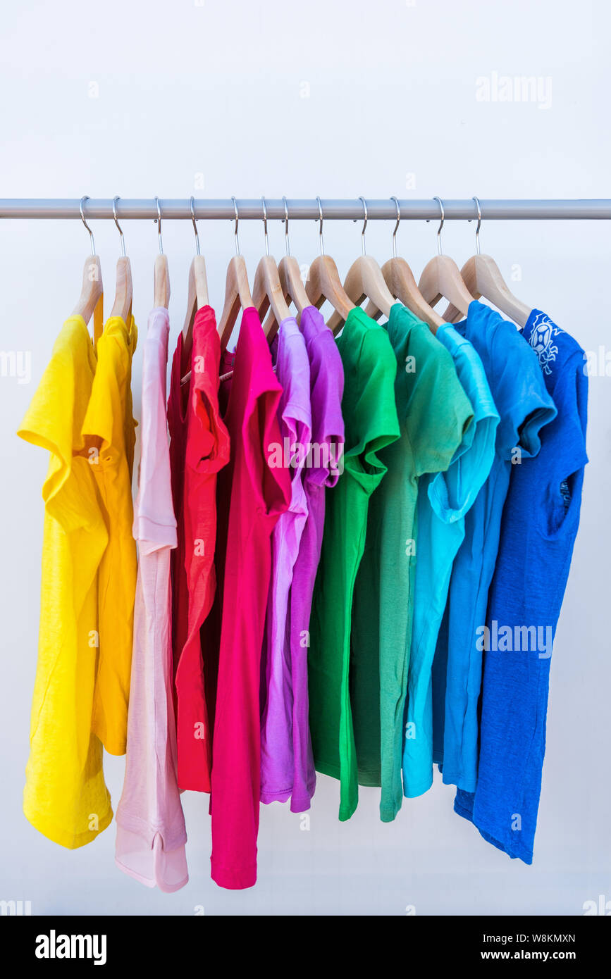 Fashion clothes on clothing rack - bright colorful stand of rainbow selection of t-shirts. Choice of trendy female wear on hangers in store closet or spring cleaning concept. Summer home wardrobe. Stock Photo