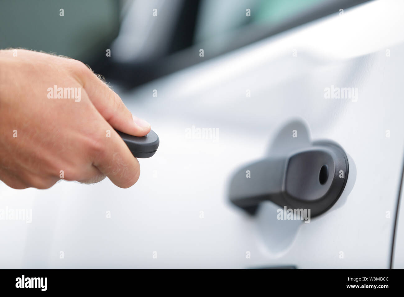 Car remote control key fob. Man driver locking doors with unlock keyless system. Person opening door starting car with starter. Hand holding key to lock doors of white car travel vacation rental. Stock Photo