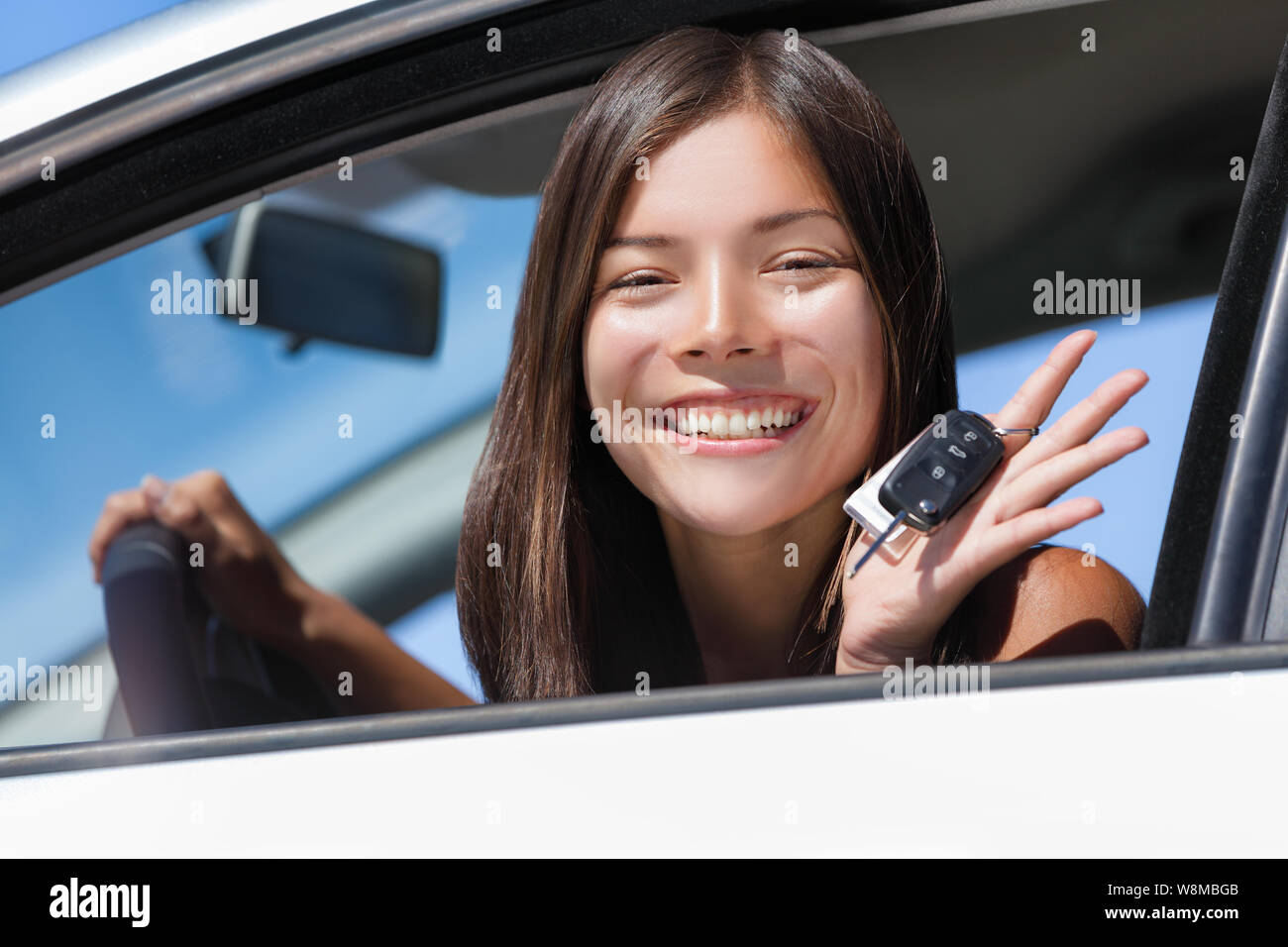 Happy Asian girl teen driver showing new car keys. Young woman smiling