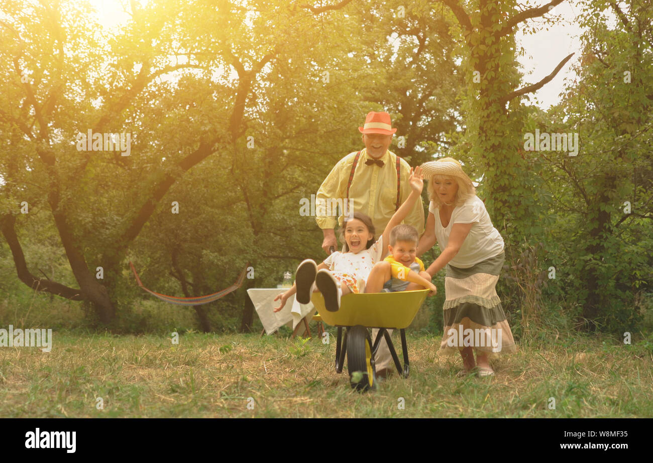 Grandma And Grandpa Are Pushing Their Grandchildren In A Wheelbarrow3 Stock Photo