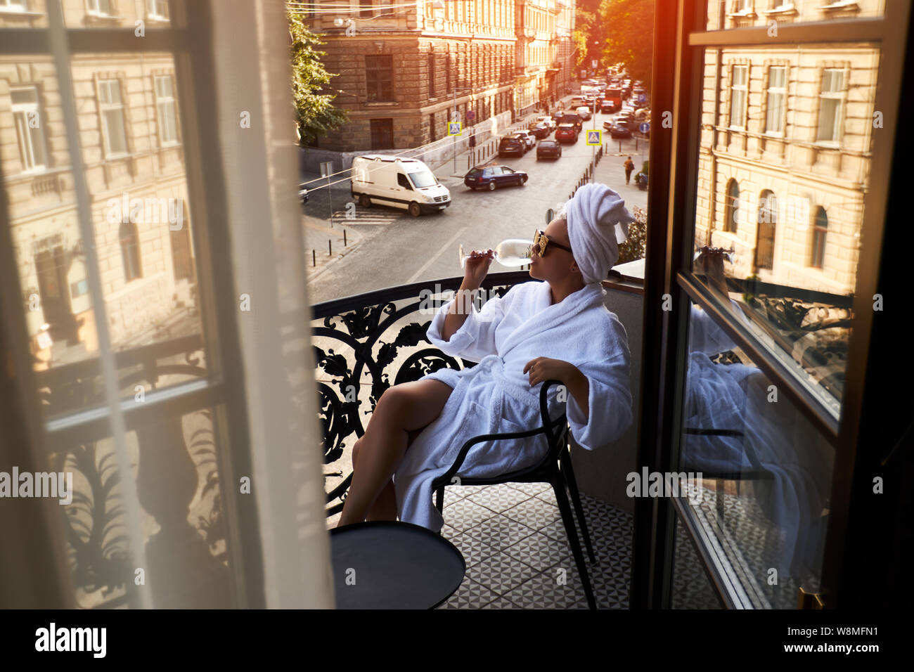 Beautiful blonde in a white coat enjoying a glass of white wine sitting on a hotel terrace against Stock Photo