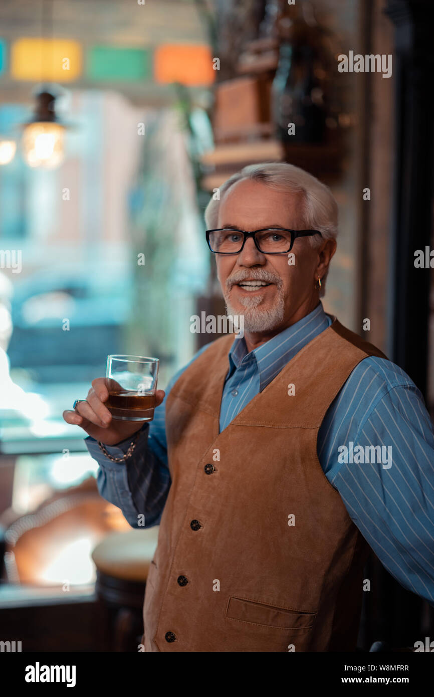 Grey-haired man wearing brown vest drinking whisky Stock Photo