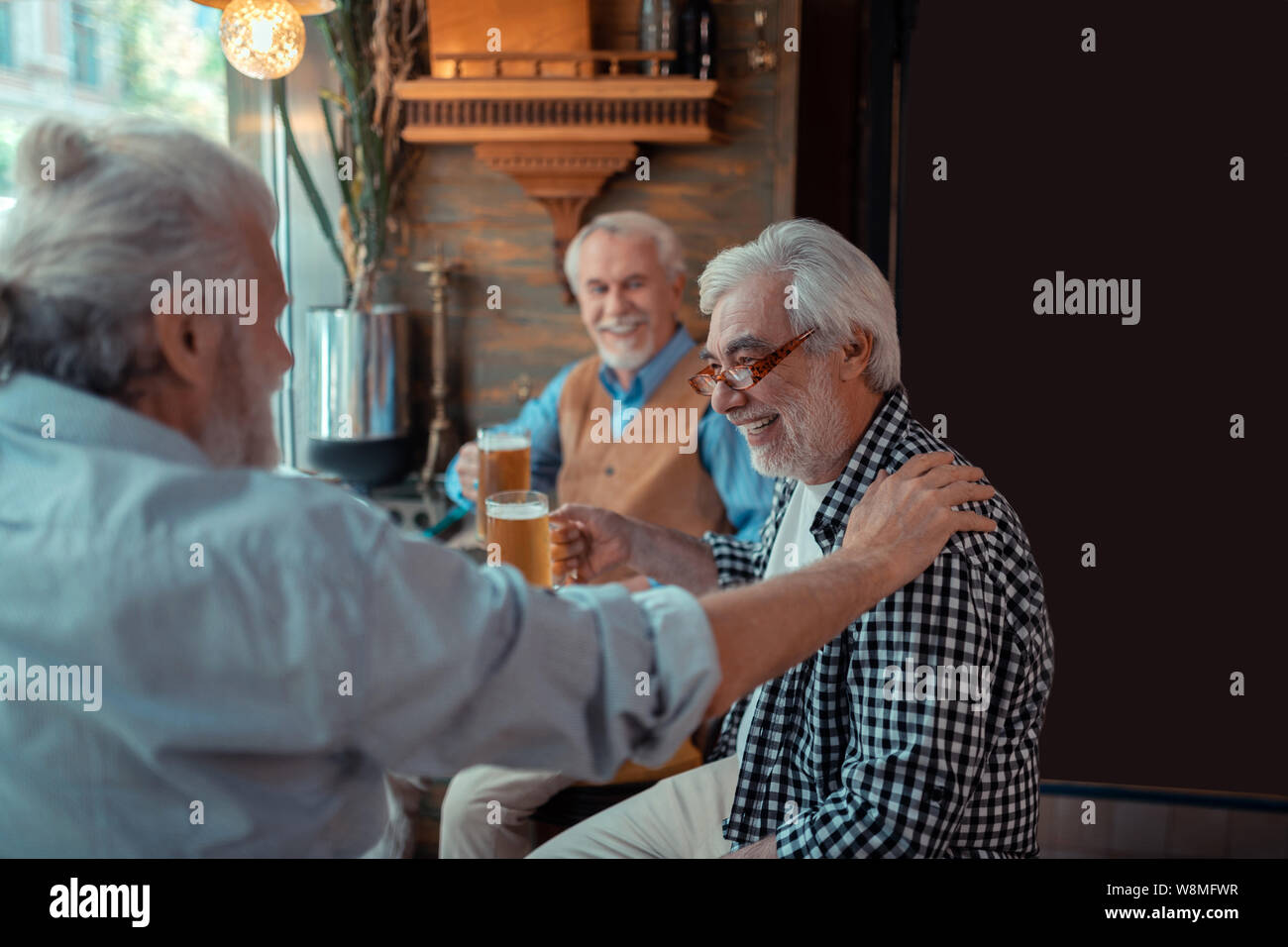 Old friend touching shoulder of man while drinking beer together Stock Photo