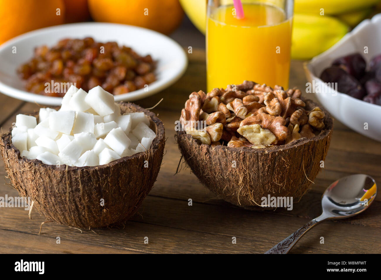 Easy raw diet breakfast. Coconut meat, walnut kernels in cups from coconut  shell. Freshly squeezed orange juice and white plate with raisins in backdr  Stock Photo - Alamy