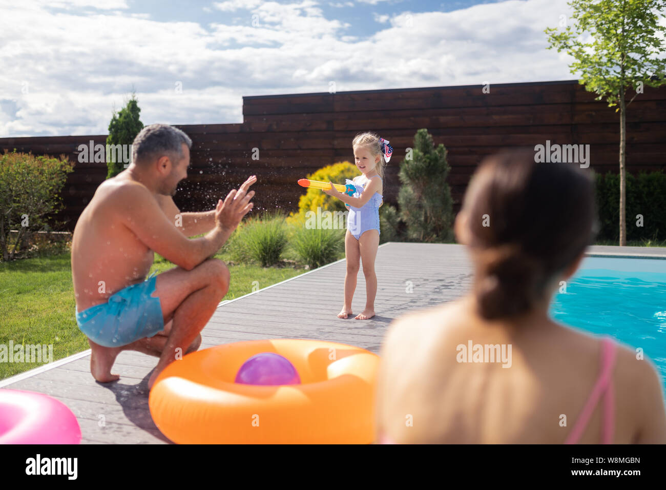 Girl using water blaster while having fun with parents near pool Stock Photo