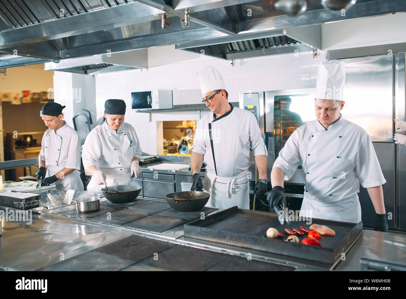 Five chefs wearing uniforms posing in a kitchen Stock Photo