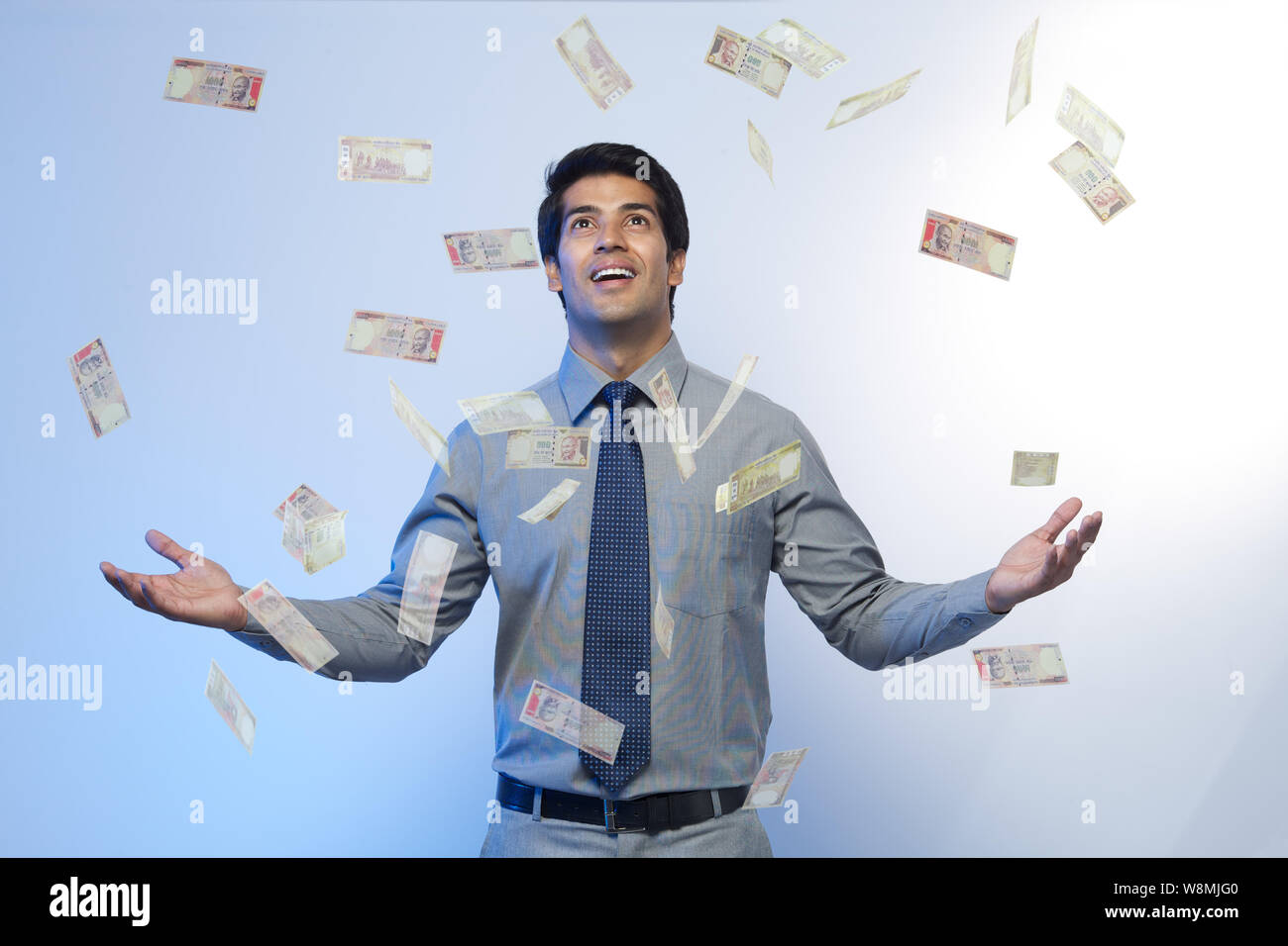 Money falling on a businessman standing with his arms outstretched Stock Photo