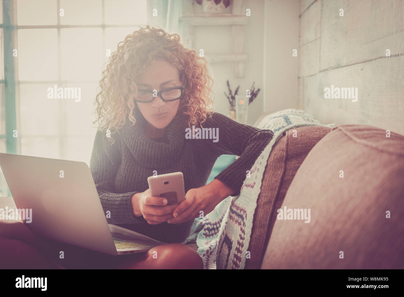 Freelance people at work at home - beautiful adult caucasian woman sit on the sofa with phone device and laptop computer working -concept. of business Stock Photo