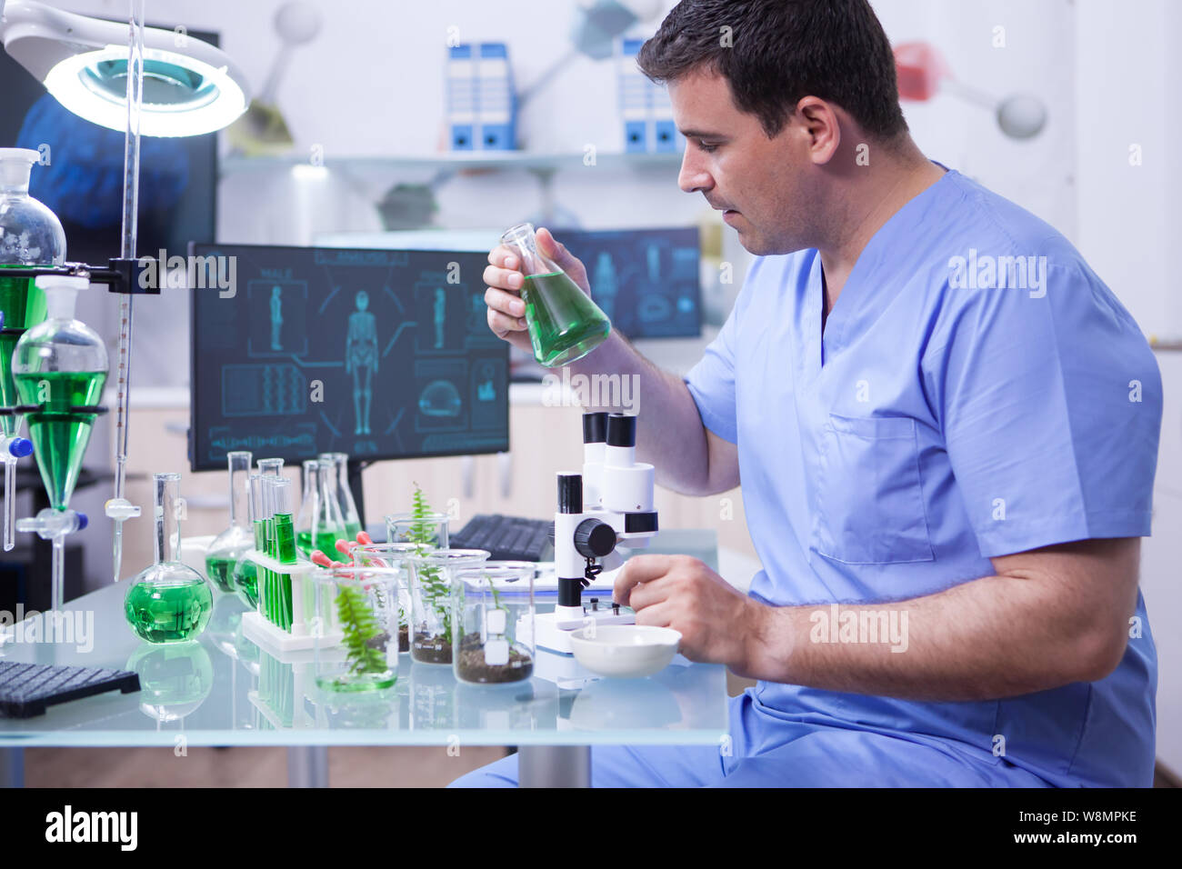 Side view of young scientific man holding a green solution in his ...