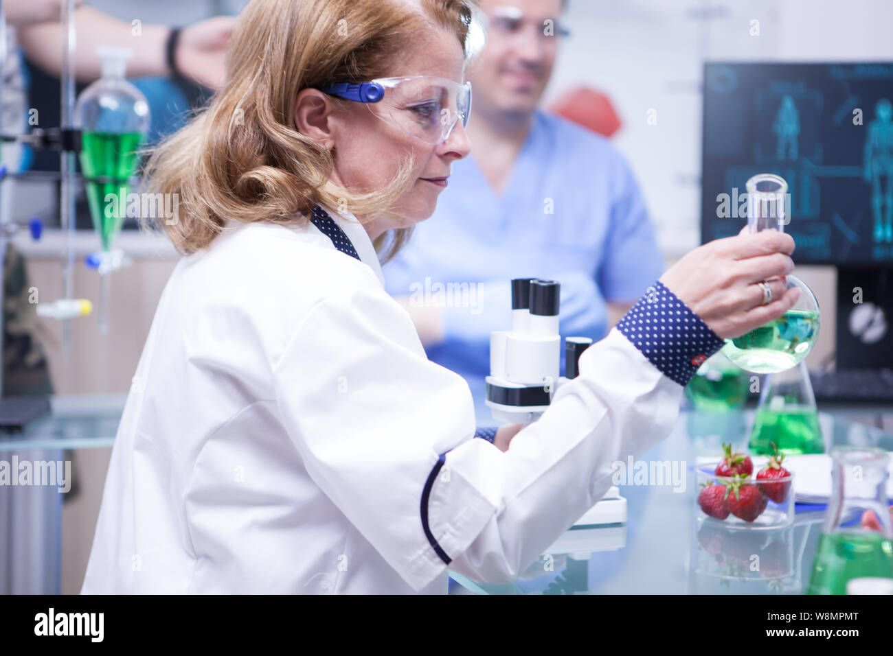 Side view of female scientist holding a test tube with green solution ...