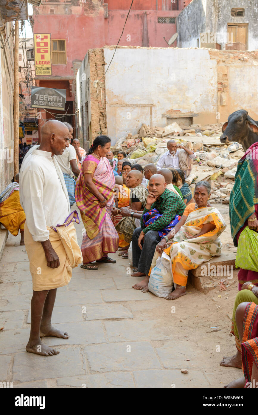 Hindu pilgrims with shaven heads sit down for a rest in a backstreet in Varanasi, Uttar Pradesh, India, South Asia. Stock Photo