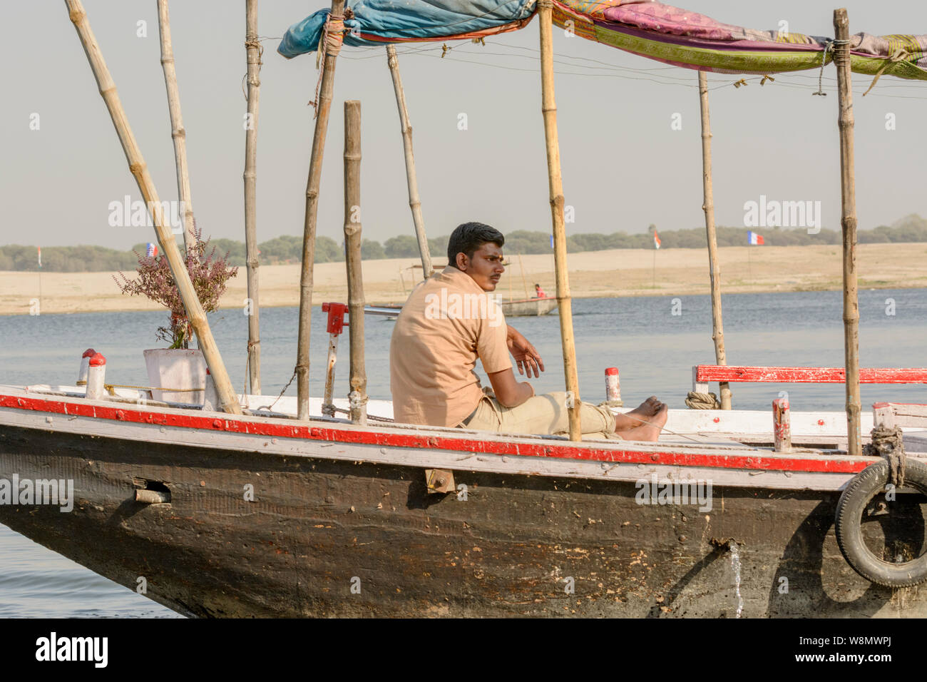 An Indian man sits on a wooden boat on the River Ganges in Varanasi, Uttar Pradesh, India, South Asia. Also known as Benares, Banaras and Kashi. Stock Photo