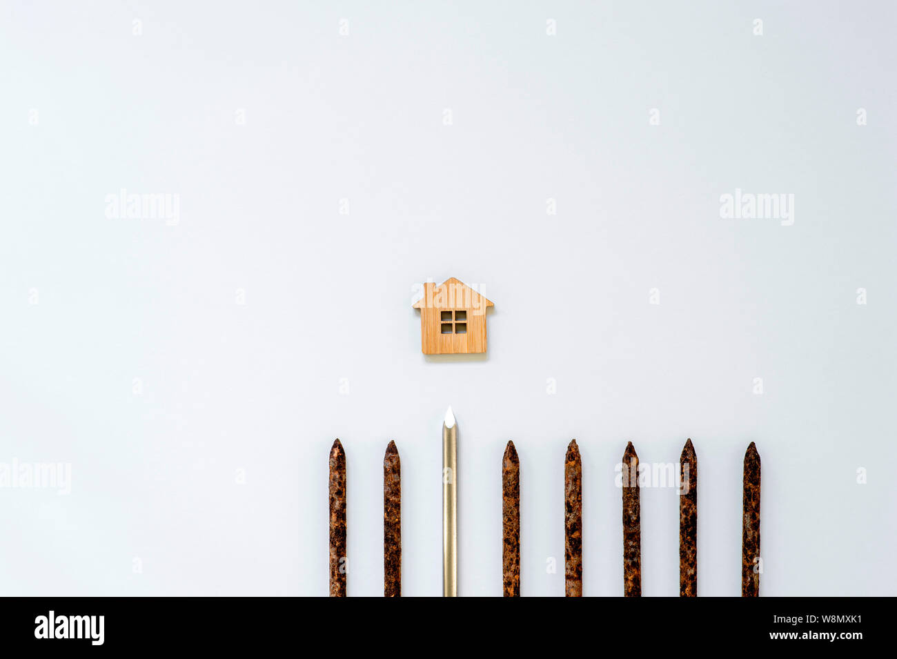 A shiny metal nail stands out in a row of old rusty nails and is aimed at the house symbol on a light background. Stock Photo