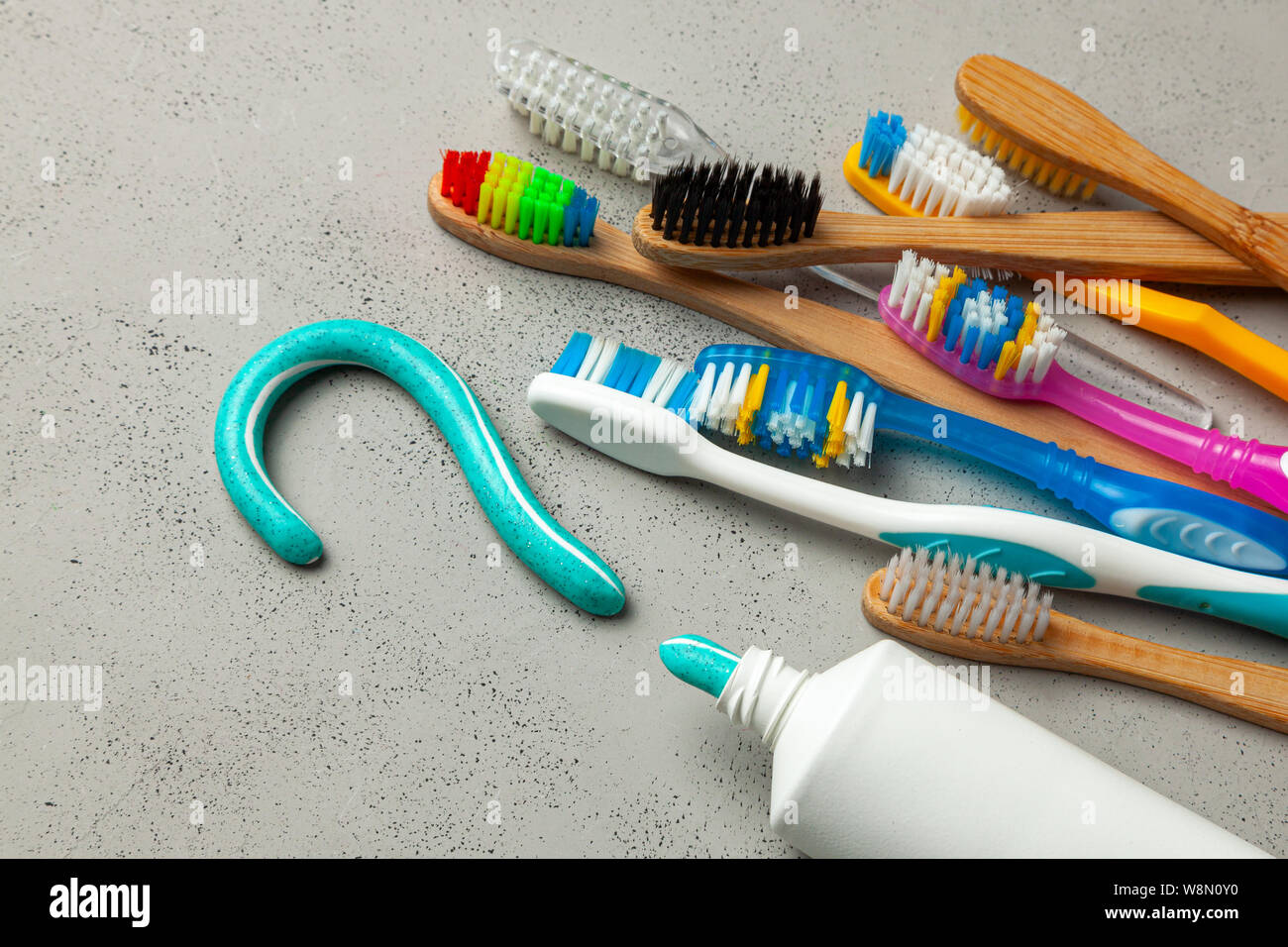 Toothpaste in the form of a question mark and many different and colored toothbrushes. Concept