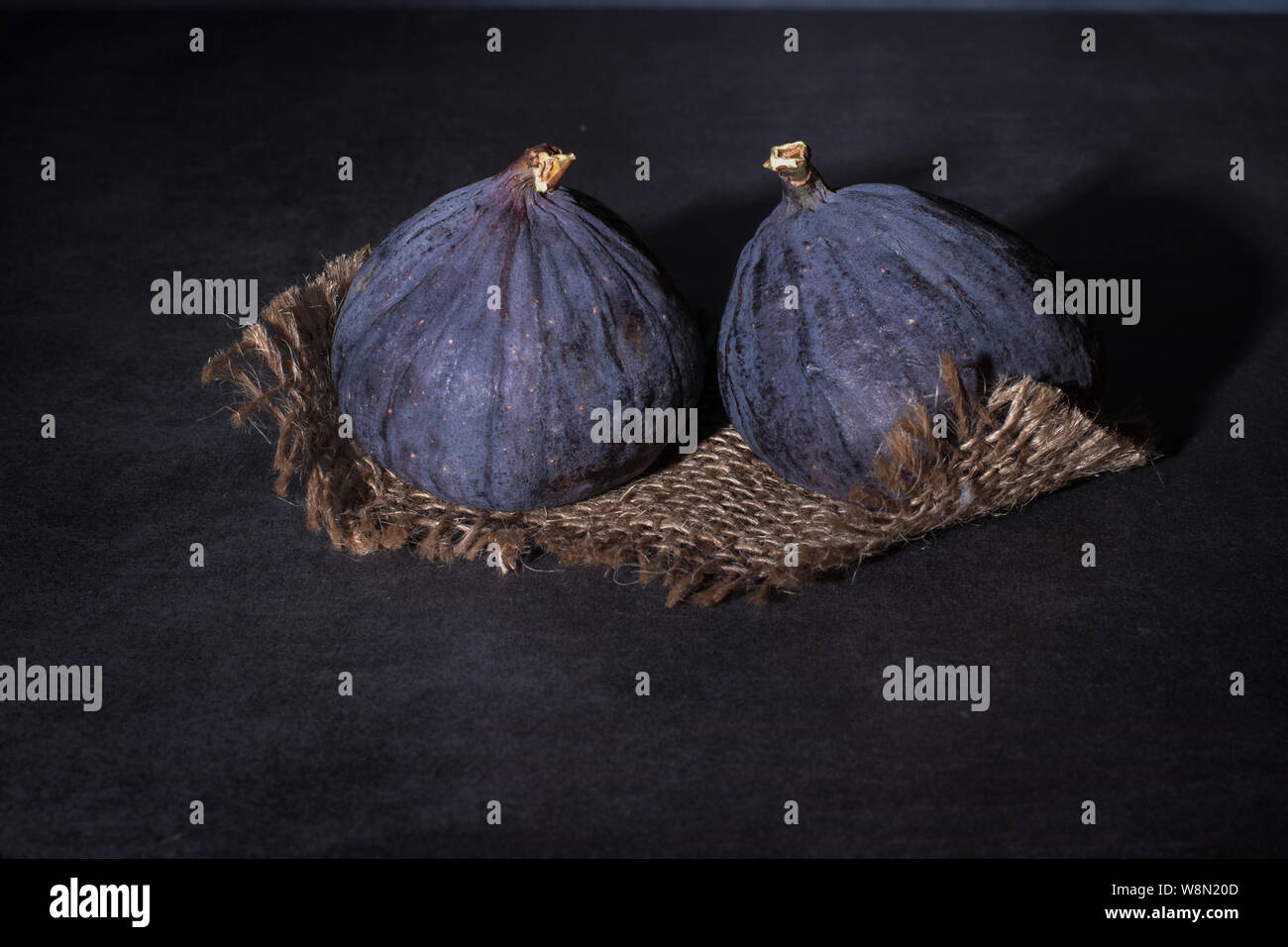 Two ripe purple figs lie on coarse cloth and on a concrete top. Stock Photo