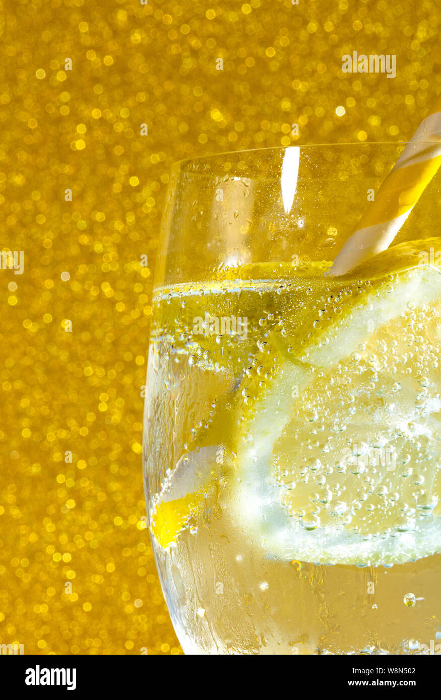 fresh soda with bubles an ice cube, a  slice of lemon and a straw on a shiny golden background Stock Photo