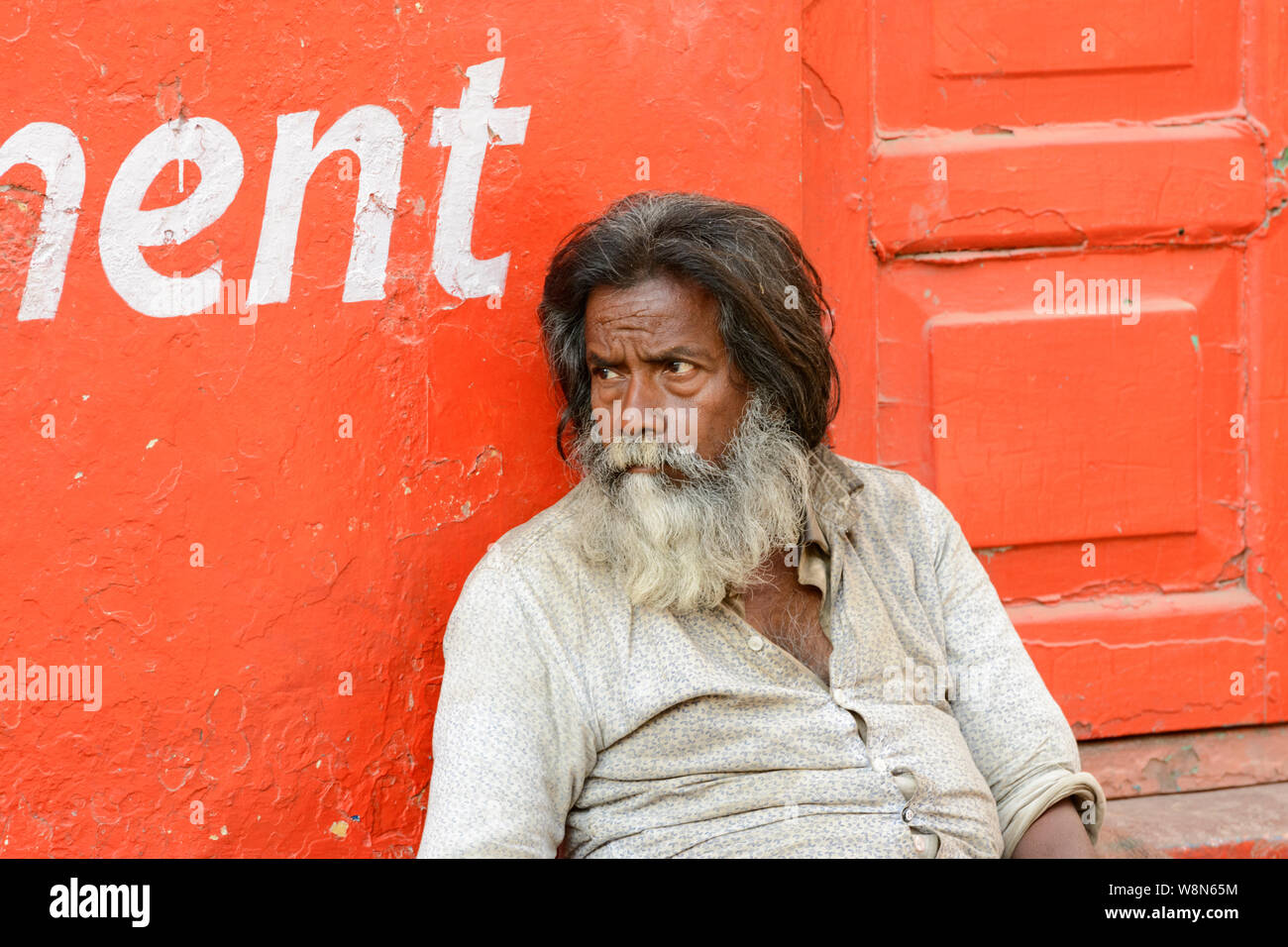 An Indian man sits on the pavement in the backstreets of Varanasi, Uttar Pradesh, India, South Asia. Also known as Benares, Banaras and Kashi. Stock Photo