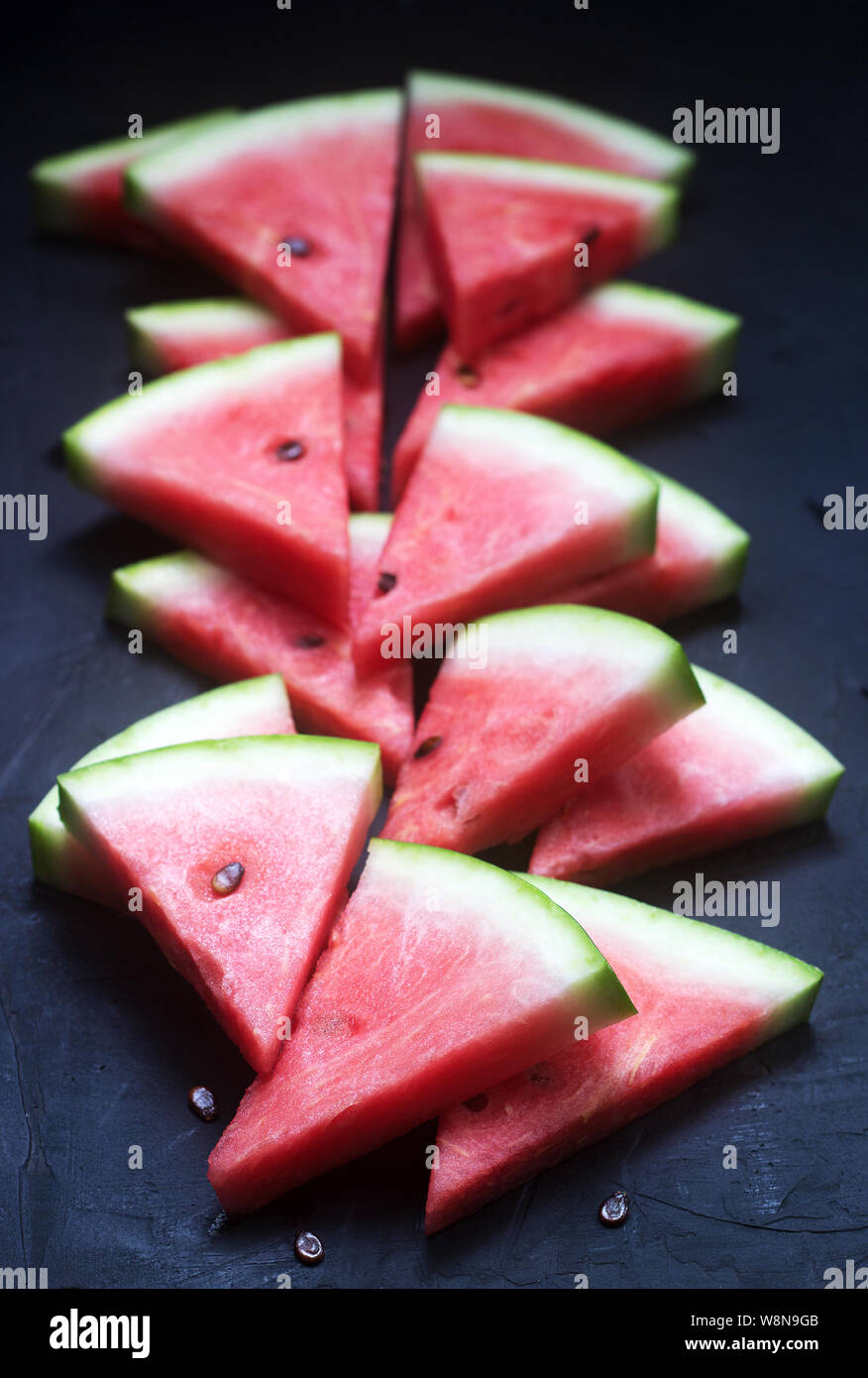 Triangular watermelon slices with seeds on a black concrete background ...