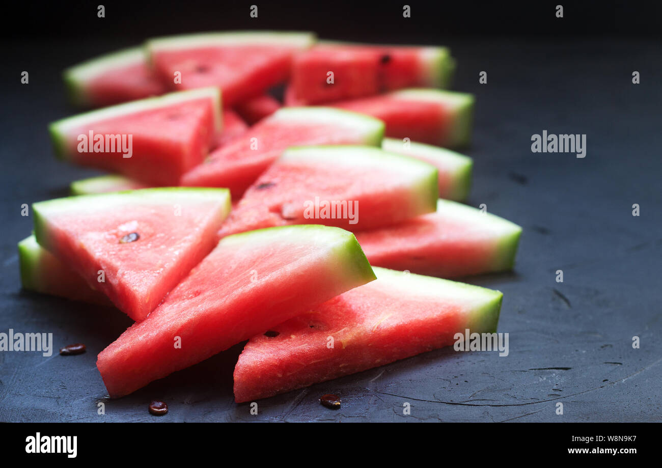Triangular watermelon slices with seeds on a black concrete background ...