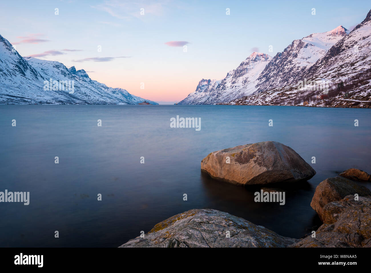 Ersfjord at sunset in winter with snowy mountains and rocks in foreground, Norway Stock Photo
