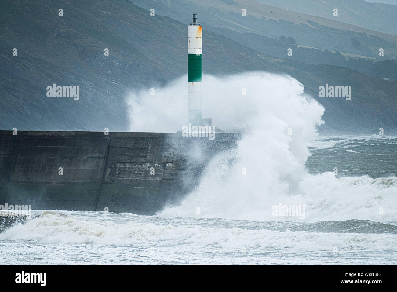 10 Aug 2019 Aberystwyth Wales UK. UK Weather: Gale force winds gusting to over 50mph and stormy seas batter the harbour lighthouse, and makes life difficult for pedestrians in Aberystwyth as unseasonably wet and windy weather sweeps across much of the west of the UK , bringing severe disruption to travel and forcing the cancellation of many outdoor events. Photo credit Keith Morris/Alamy Live News Stock Photo