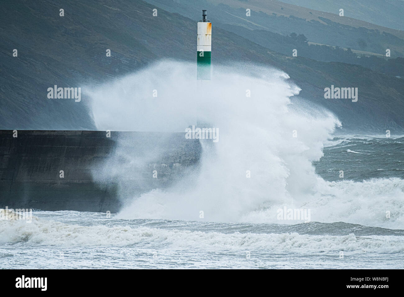 10 Aug 2019 Aberystwyth Wales UK. UK Weather: Gale force winds gusting to over 50mph and stormy seas batter the harbour lighthouse, and makes life difficult for pedestrians in Aberystwyth as unseasonably wet and windy weather sweeps across much of the west of the UK , bringing severe disruption to travel and forcing the cancellation of many outdoor events. Photo credit Keith Morris/Alamy Live News Stock Photo