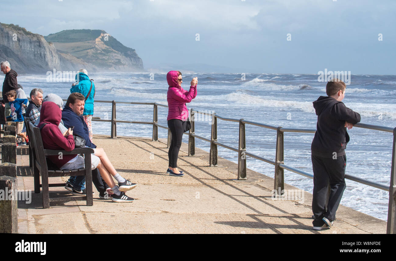 Charmouth, Dorset, UK. 10th August 2019. UK Weather:  Holidaymakers venture out on a blustery day at the seaside village of Charmouth as the unseasonably strong south-westerly winds continue to batter the South West Coast on Saturday afternoon. Yellow warmings for high wind have been issued across the South West. Credit: Celia McMahon/Alamy Live News. Stock Photo