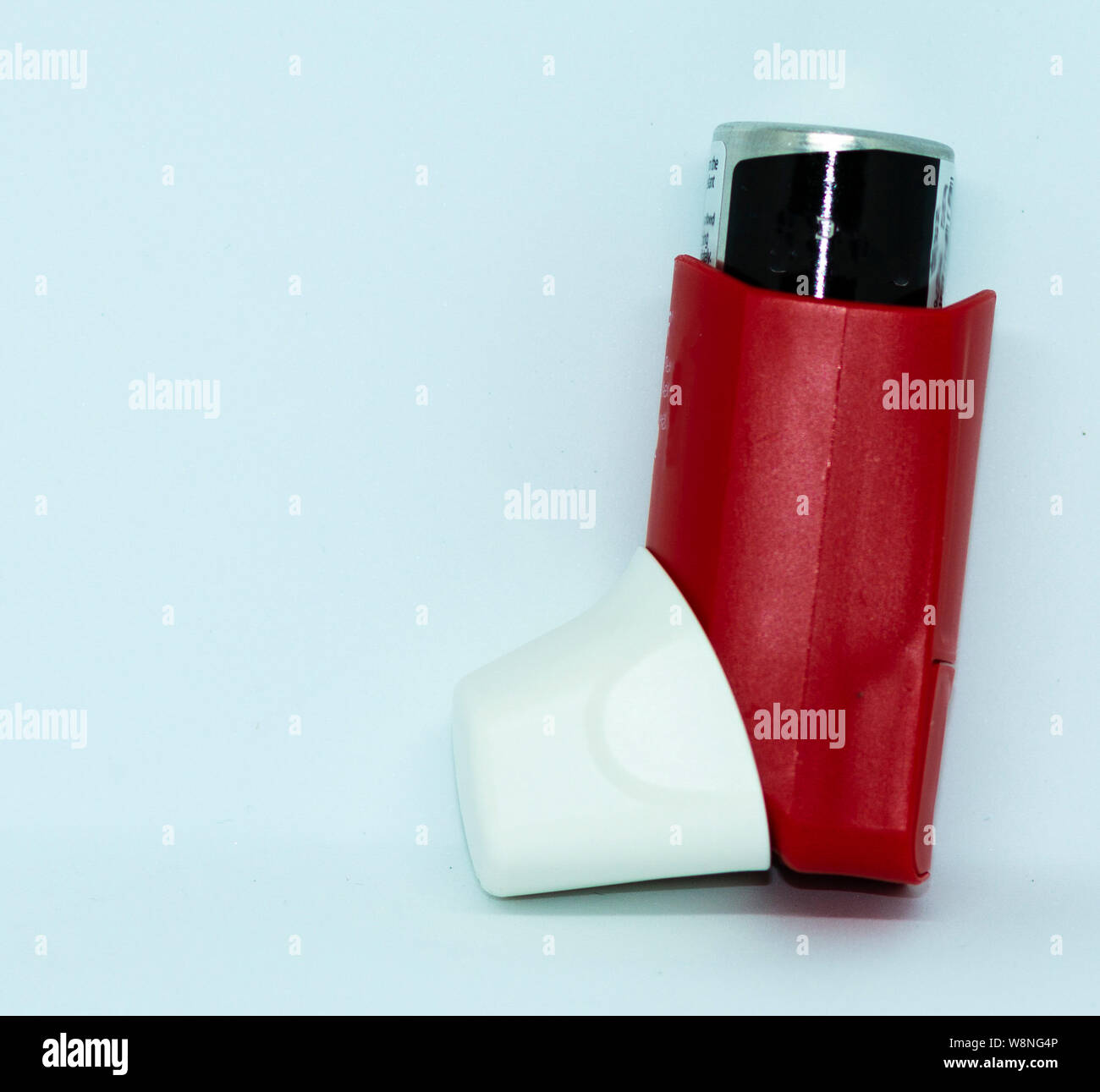 A red and white asthma rescue inhaler standing in front of a white ...