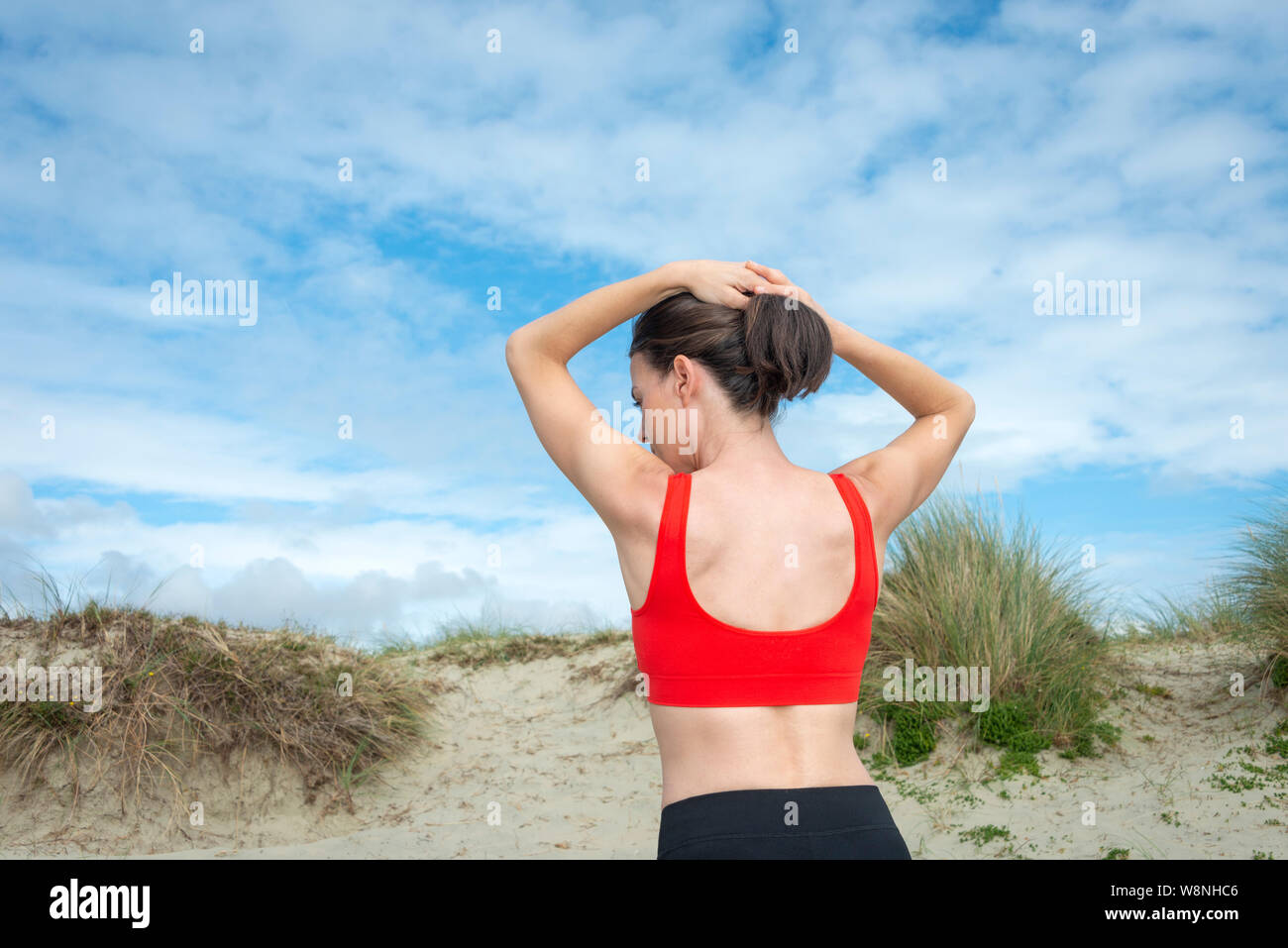 woman wearing a red sports bra adjusting her hair, back view. Stock Photo