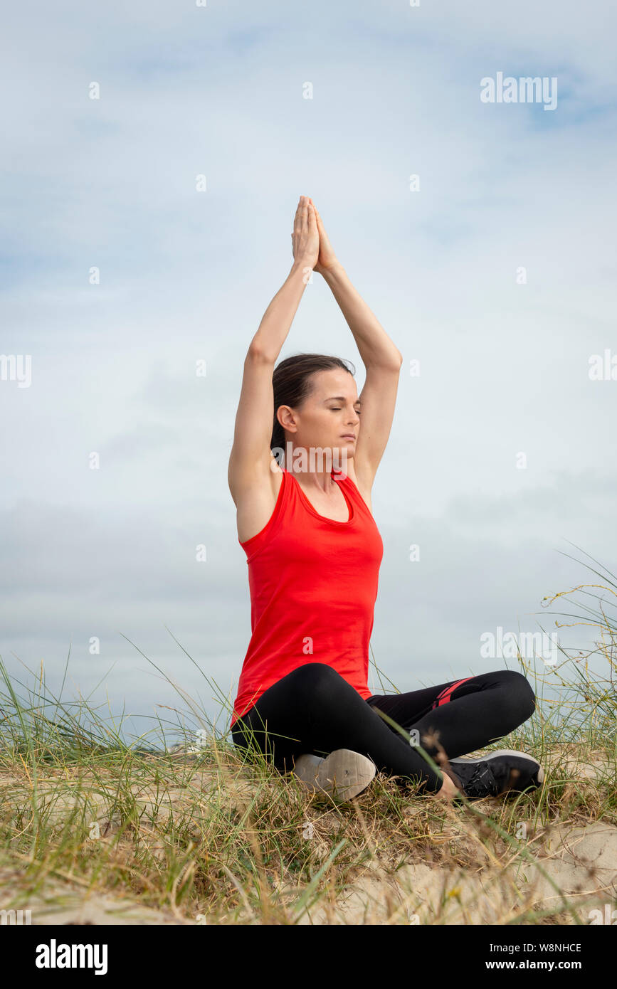 Woman sitting crossed legged and meditating, practicing yoga outside. Stock Photo