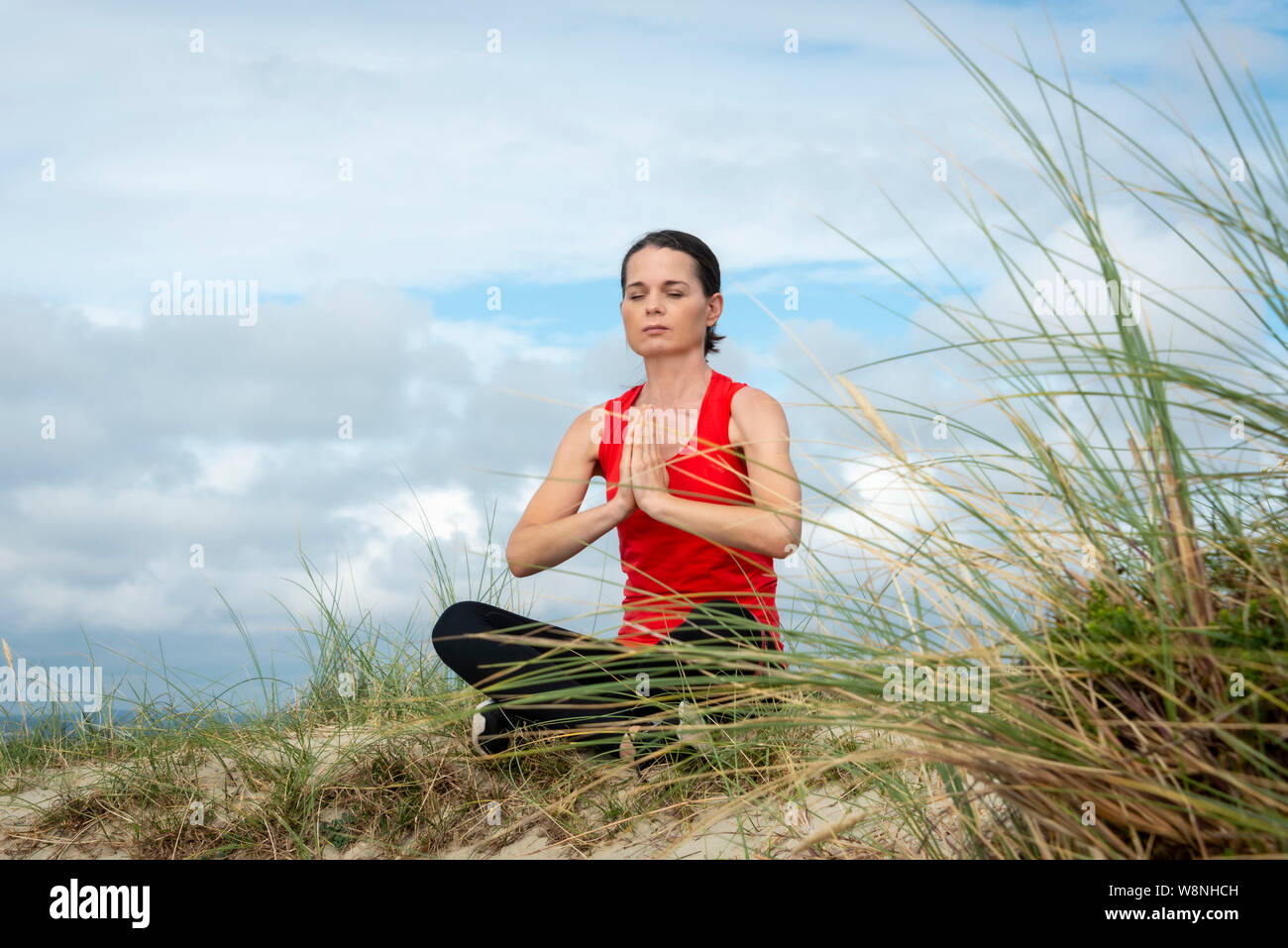 Woman sitting crossed legged and meditating, practicing yoga outside. Stock Photo