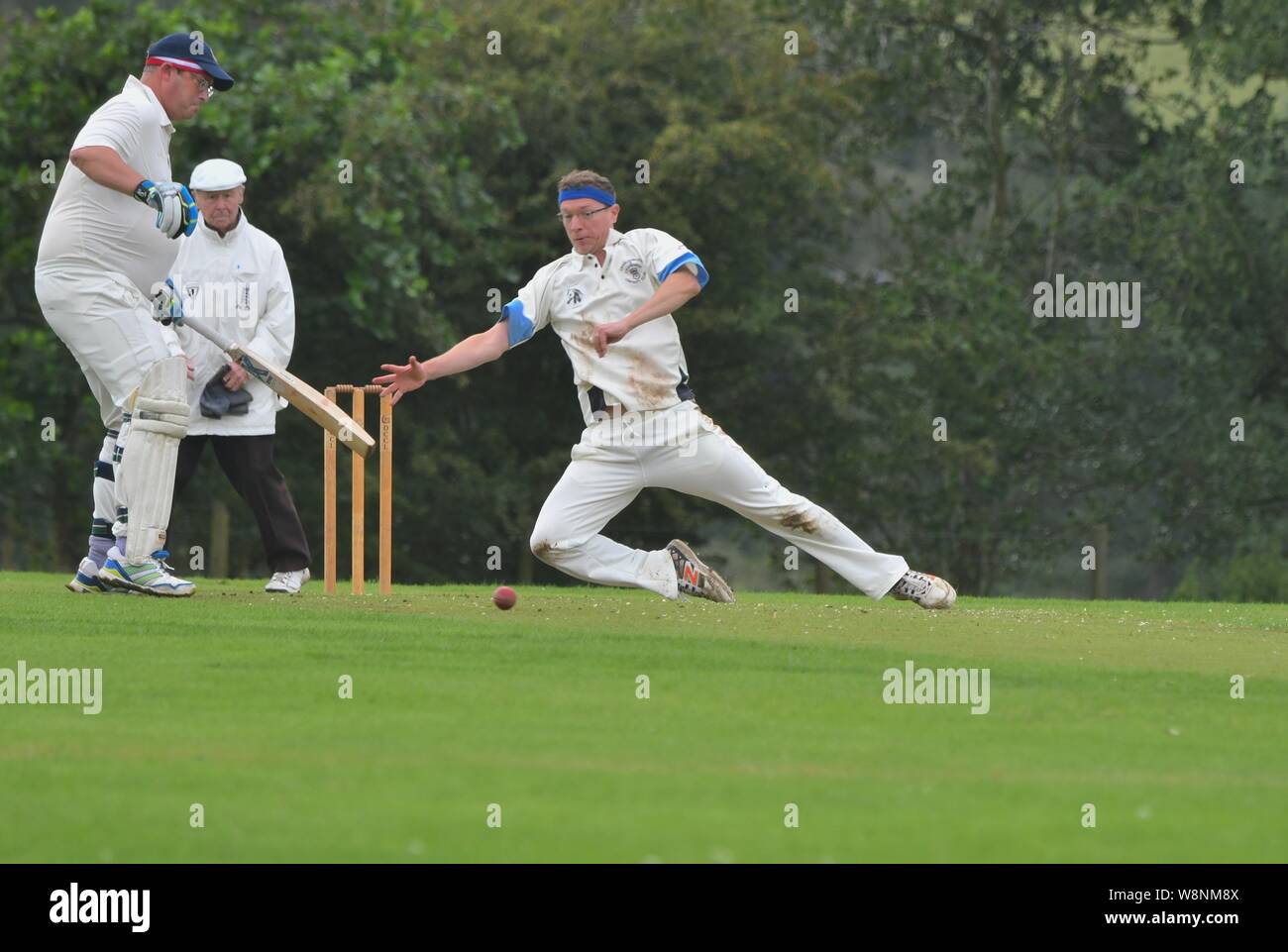 A bowler tries to stop the ball passing him in the match between Charlesworth and Chisworth CC and Mottram 2nd team Stock Photo