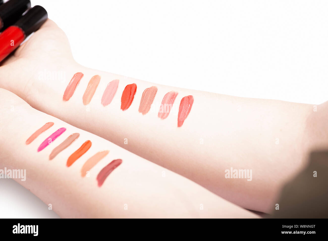 Woman hands with lipstick test strokes holding lip gloss containers, lipstick swatches on female arm Stock Photo