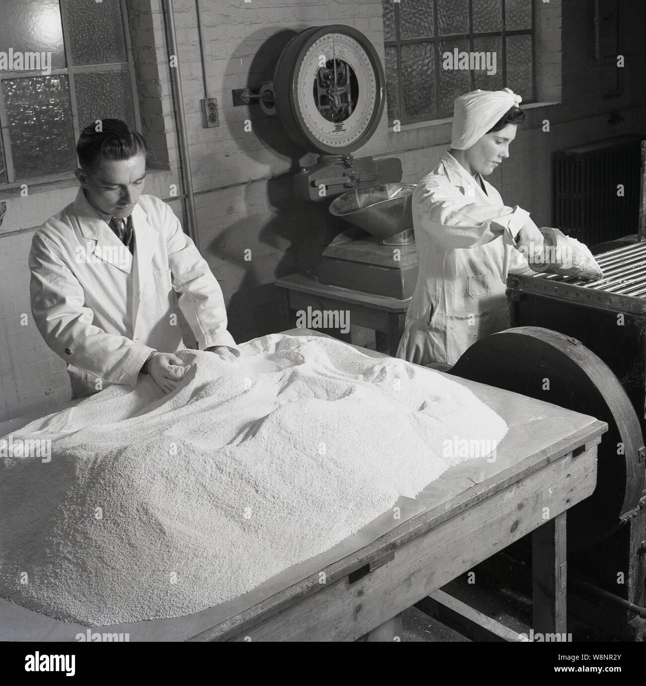 1950s, historical, a male and female wearing white-coats working at the medical supplies business of Arthur H. Cox & Co. They are processing the raw materials for pills. Established in Brighton, England in 1839, their advertising strapline was, 'The Foremost Tablet House'. Arthur Hawker Cox was a successful Victorian businessman who in 1854 patented a pearl coating for pills. As a manufacturer of pharmaceuticals they supplied chemists thorougout the UK and the commonwealth. Stock Photo