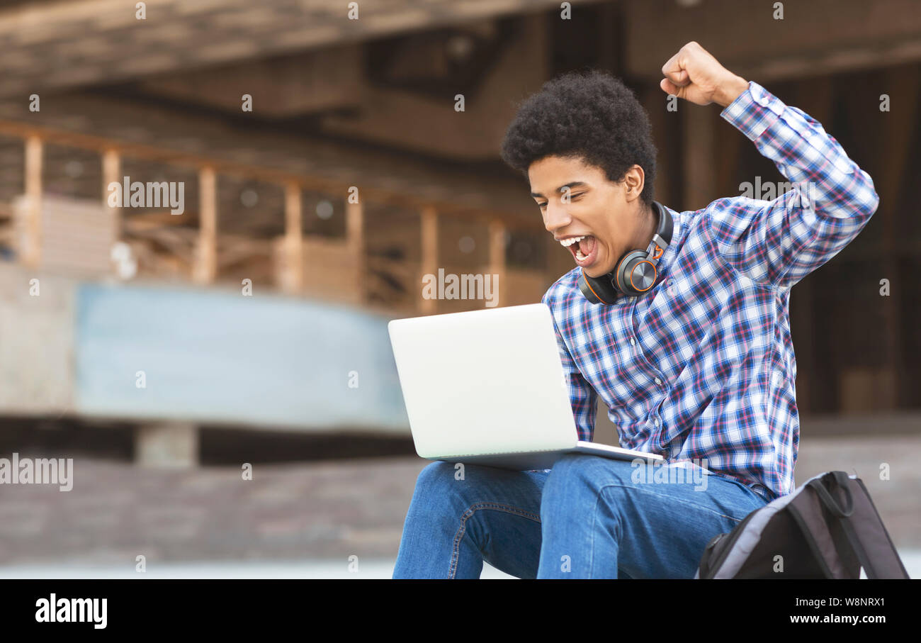 Excited young guy celebrating victory with laptop outdoors Stock Photo