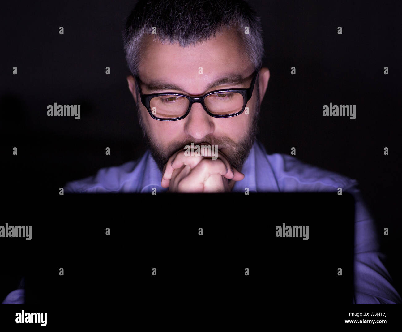 Puzzled man looking at laptop screen in dark room Stock Photo Alamy