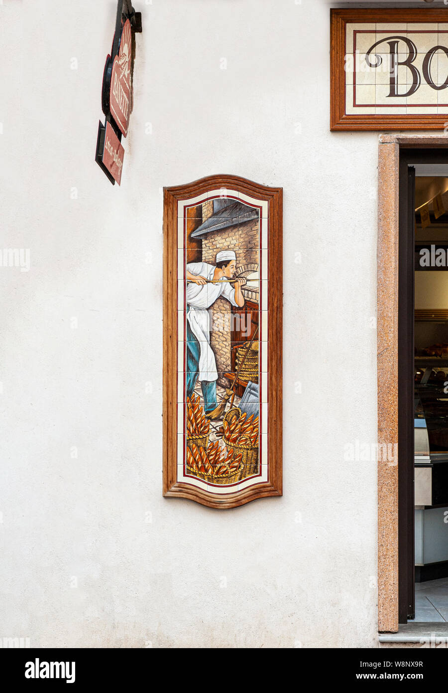 Tiled Plaque outside Baker's Shop in Calvi, Corsica, showing the baker loading bread into the oven Stock Photo