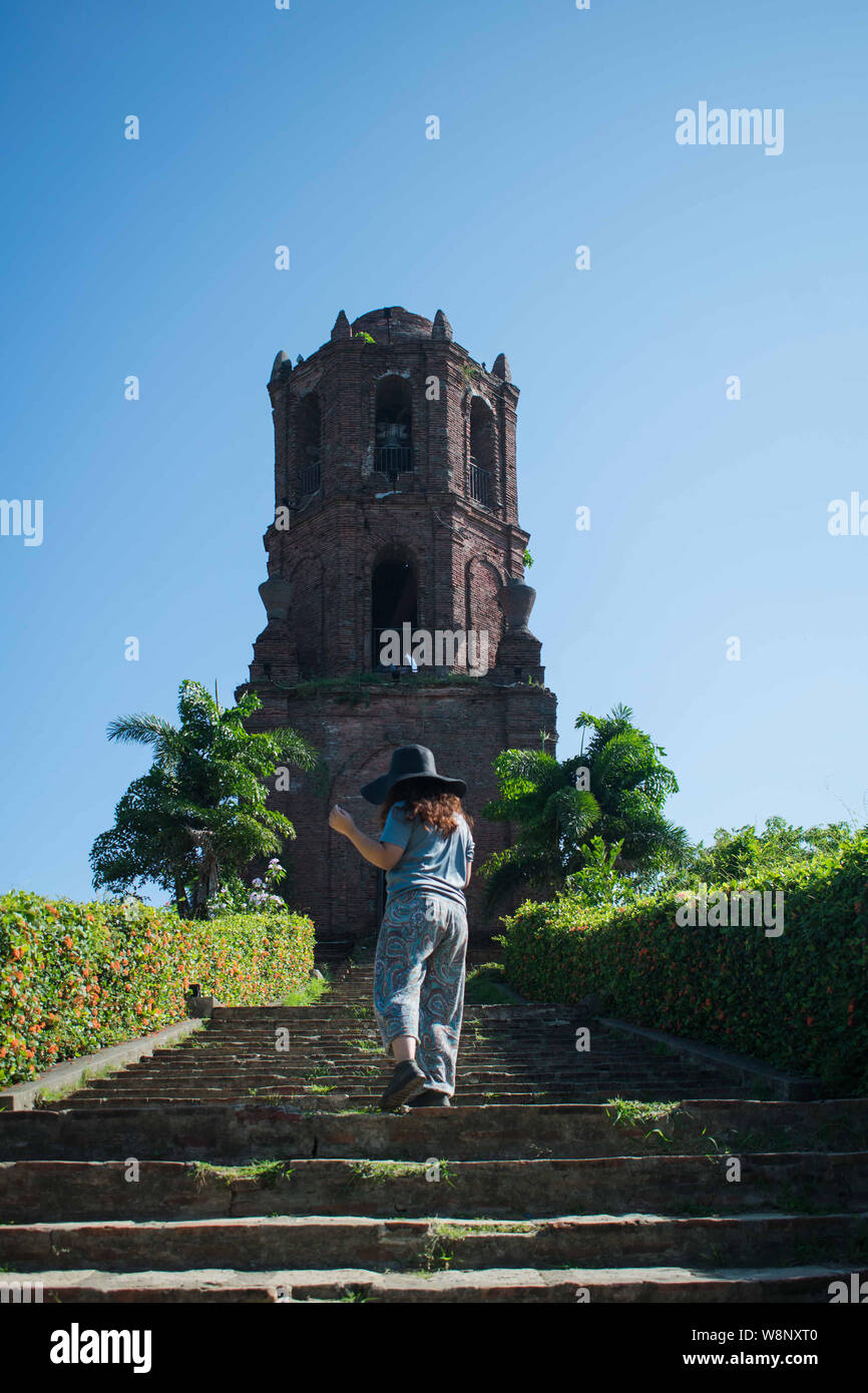Woman with her back at the camera going up the stairs to an ancient belltower in Vinga Philippines Stock Photo