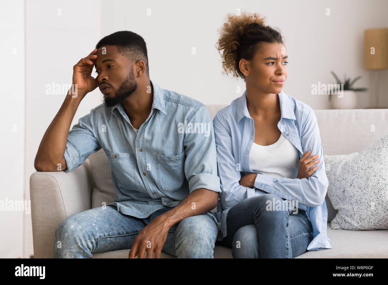 Upset Black Couple Avoiding Eye Contact Sitting On Couch Stock Photo